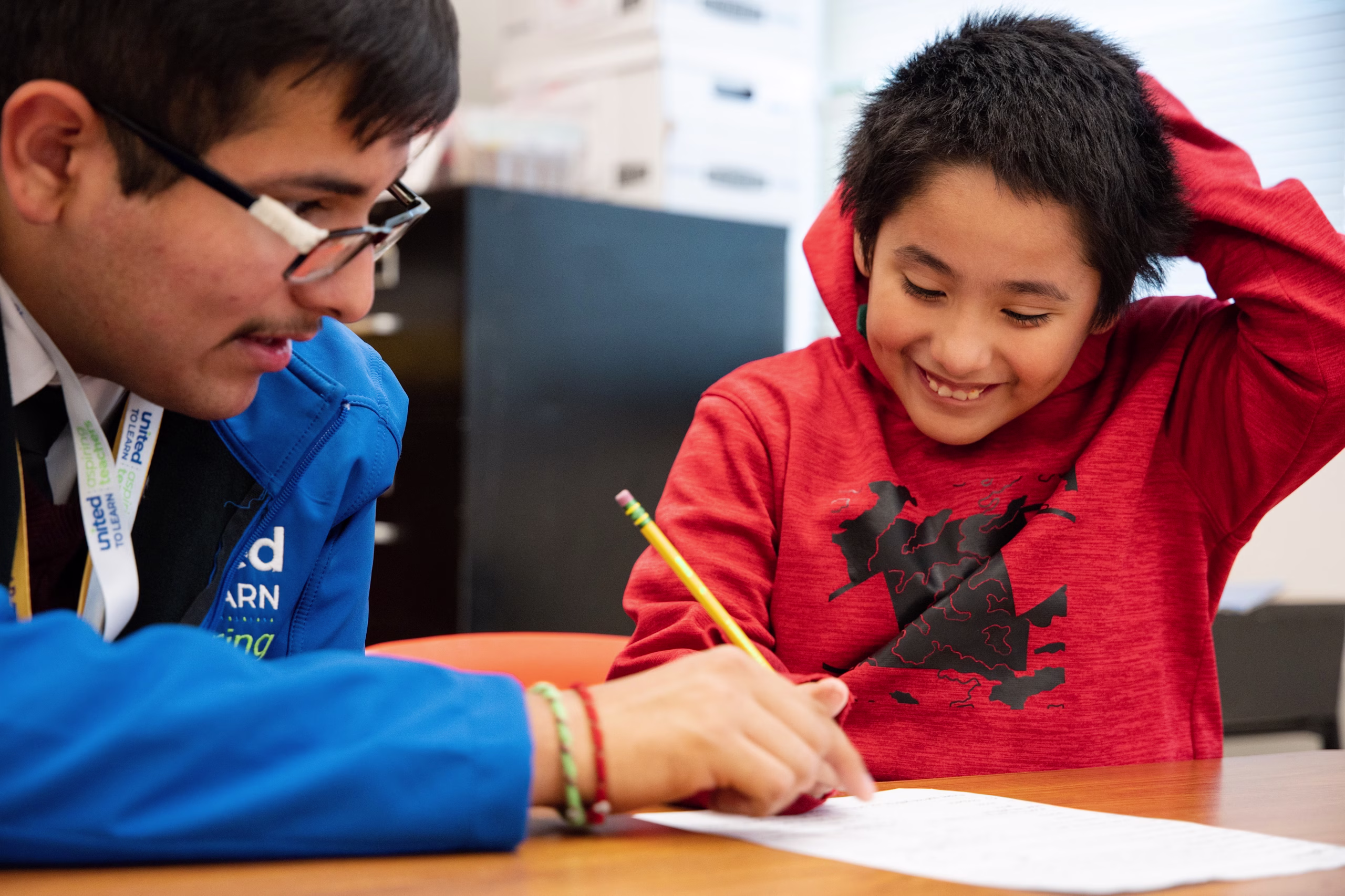 Our Commitment a boy is smiling while he works with his tutor